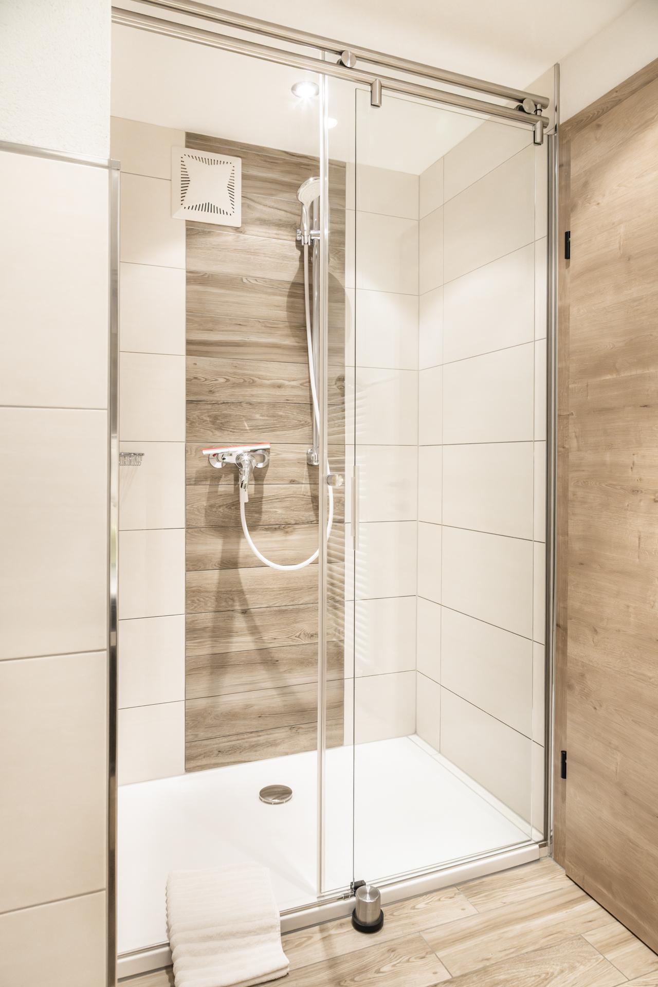 A modern shower with glass partition and bright tiled floor. The walls are decorated in neutral colors, creating a calming atmosphere.