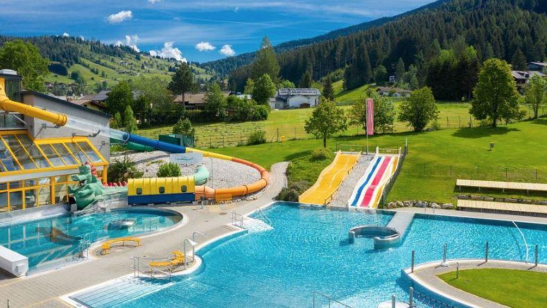 A beautiful water park with a large swimming pool and various slides. Surrounded by green hills and a blue sky.