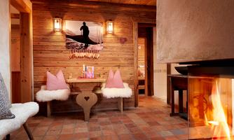 Experience pure coziness and alpine charm. The open fireplace spreads comforting warmth while you relax on the wooden benches covered with lambswool. Rustic wooden walls, traditional decorative elements, and soft candlelight create a snug atmosphere – the perfect place to unwind after an extensive sauna session. A place where heart and soul find peace. Cozy wellness area with an open fireplace, adjacent to the sauna.