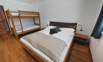 A modern bedroom with a double bed and a bunk bed. The room has a warm wooden floor and is designed to be bright and friendly.