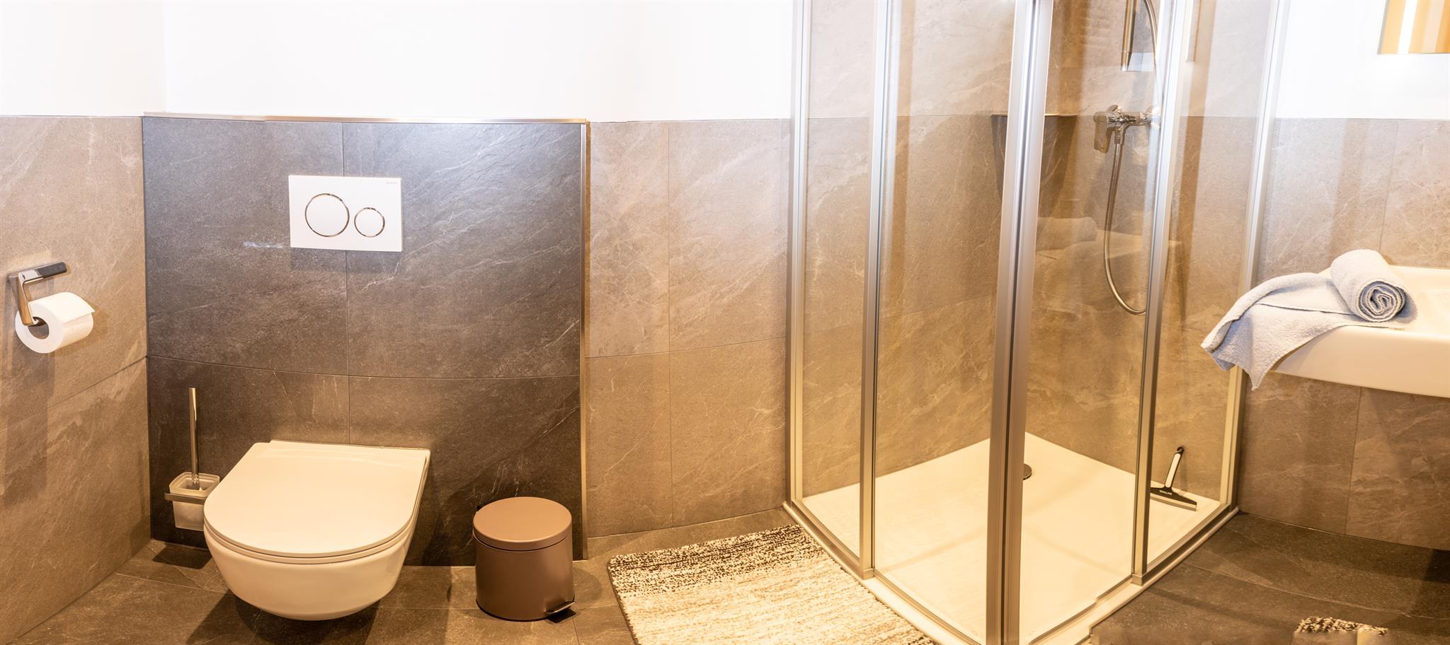 A modern bathroom with a shower and a toilet. The walls are partially painted in neutral tones, and towels are ready.