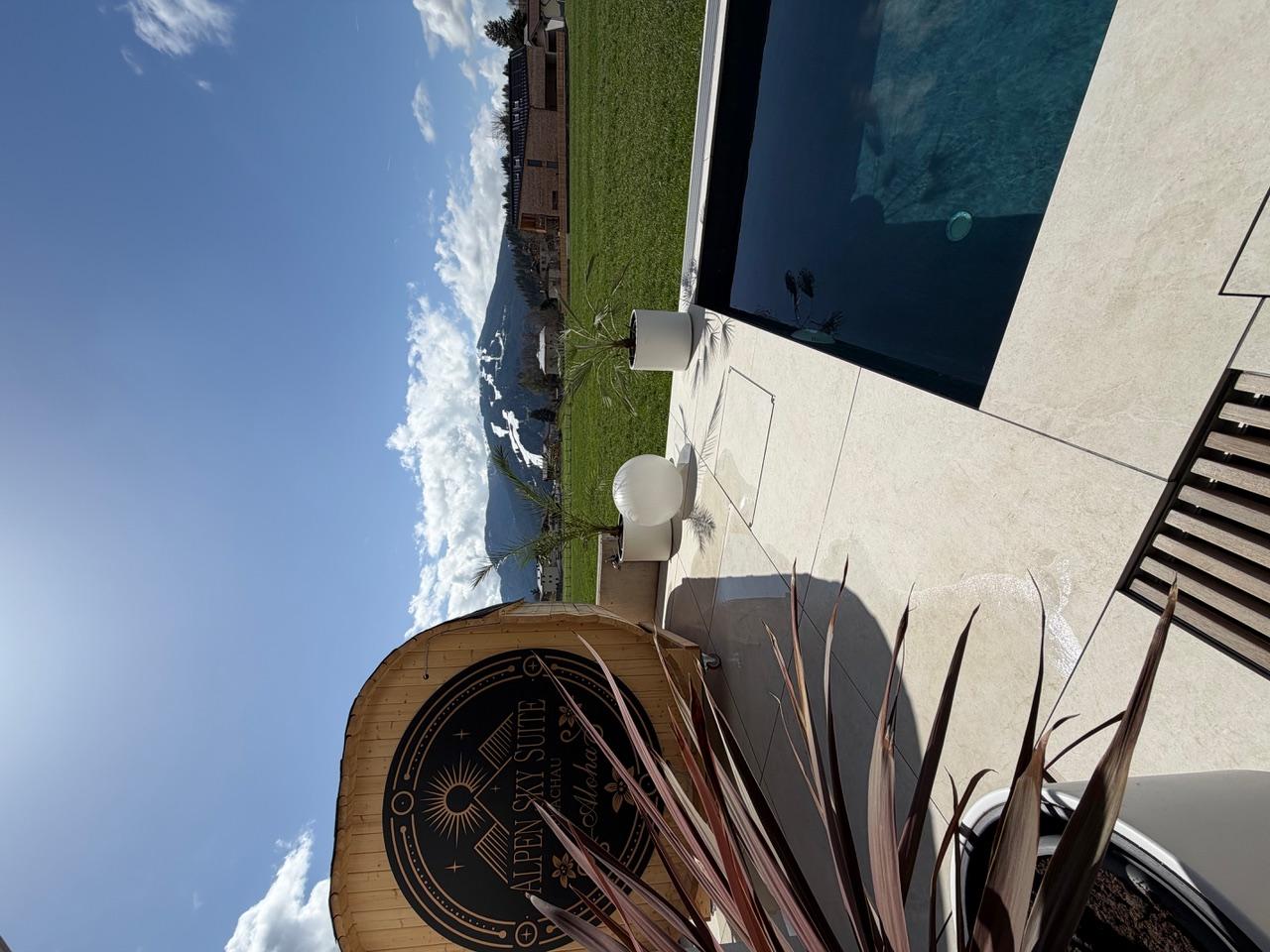 A modern terrace with a swimming pool, sauna, and mountain view. The clear view and sunny atmosphere create a relaxing mood.