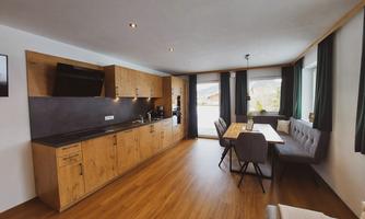 A modern kitchen with wooden cabinets and a cozy dining area. Large windows provide plenty of daylight and a view outside.