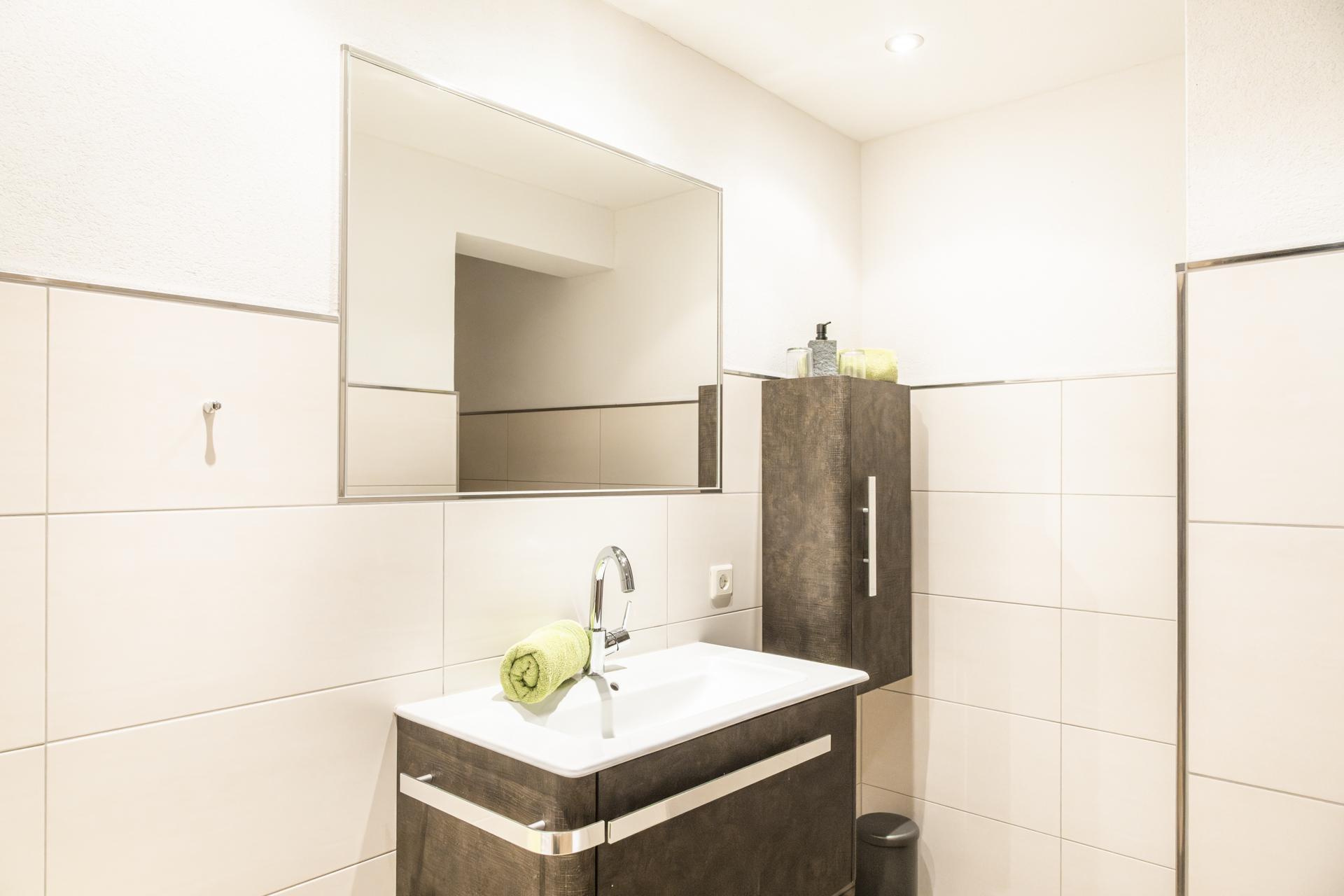 A modern bathroom with a sink and a large mirror. The walls are brightly tiled and there are some decorative elements such as a towel.
