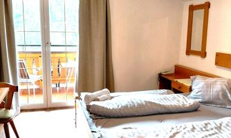 A bright bedroom with a double bed and a large window. On the balcony, there are chairs and a table.
