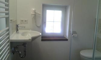 A modern bathroom with a sink, a toilet, and a shower. A small window lets in natural light.