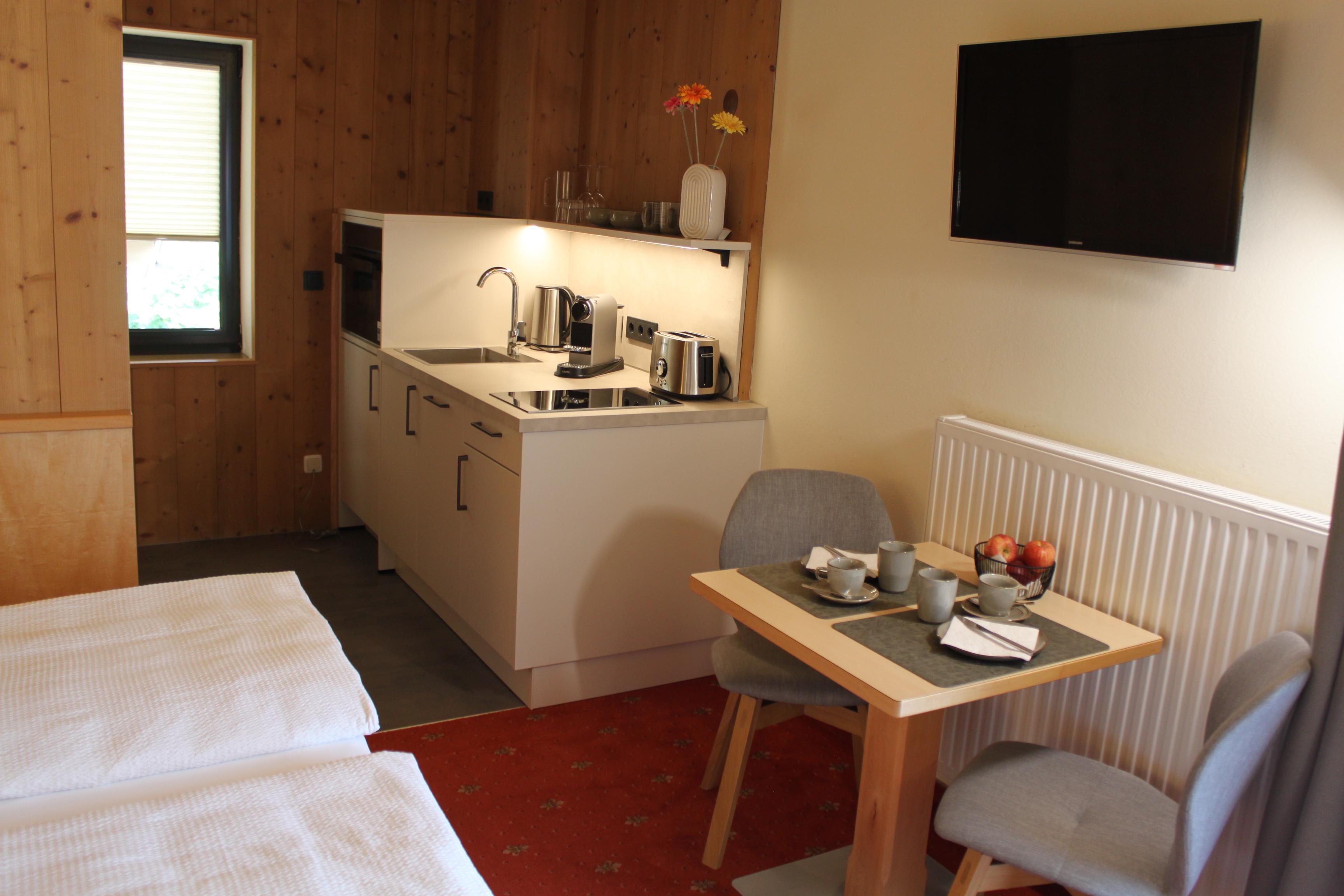A cozy room with a double bed and a small kitchenette. A set table and a television on the wall complete the atmosphere.