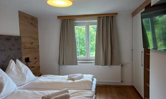 A bright room with a double bed and a large window. The walls are subtle and there is a modern decor.