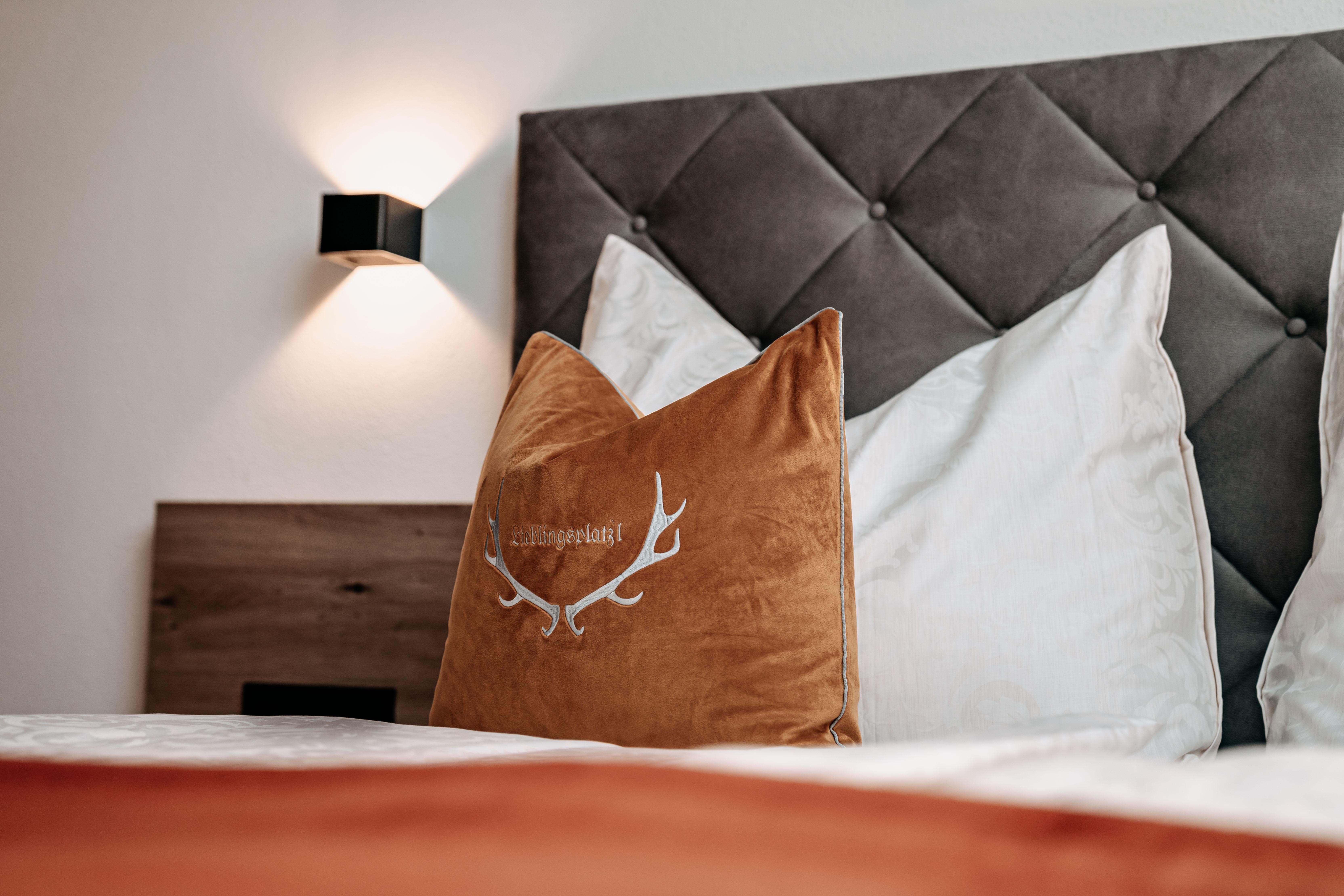 A stylish bedroom with a padded headboard and cozy cushions. The warm lighting and earthy tones create an inviting atmosphere.