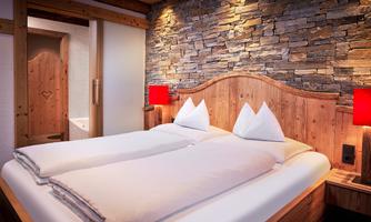 Comfortable bedroom! This cozy bedroom impresses with its stylish combination of rustic stone wall, warm reclaimed wood, and modern accents. The spacious double bed with thoughtful details ensures restful nights. Particularly convenient: The bathroom with bathtub is directly accessible from the bedroom – ideal for relaxing wellness moments in a private atmosphere. A place to feel good and unwind.