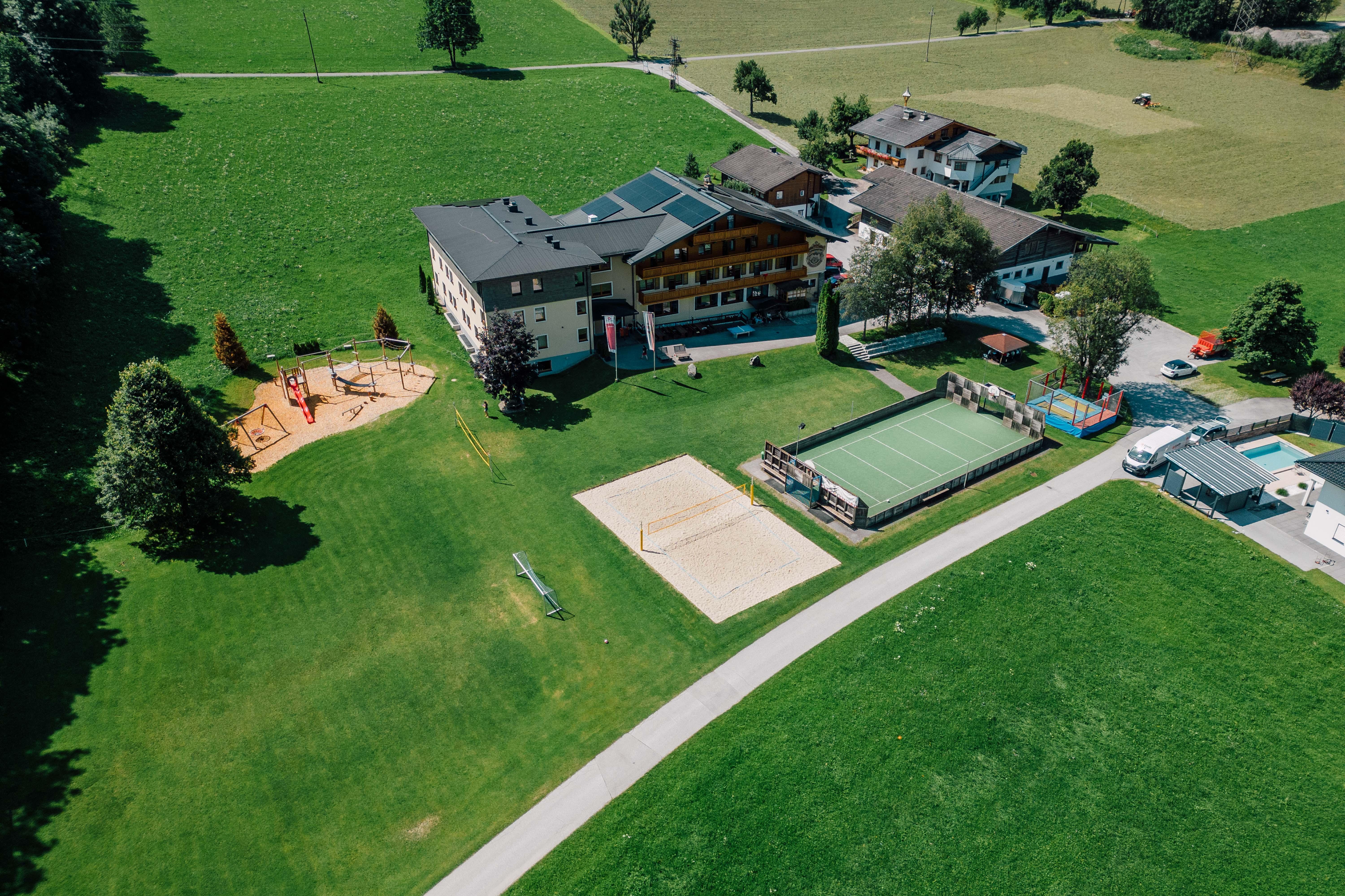 A vast green area with a playground, sports field, and several buildings. The surroundings depict a peaceful rural landscape with trees and meadows.