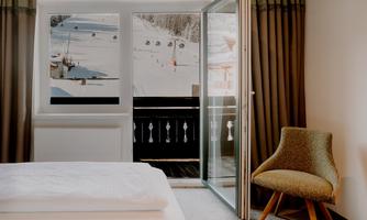 A cosy hotel room with a view of the ski slope and snow-covered mountains.