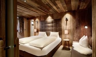 Comfortable bedroom with reclaimed wood, elegant design, and an additional bed. This stylish bedroom combines alpine charm with thoughtful functionality. The large double bed with a padded leather headboard ensures restful sleep, while warm reclaimed wood paneling and atmospheric lighting create a cozy atmosphere. Practical: The sofa placed at the side can be used as an additional bed if needed – ideal for families with a child or extra guests. A cozy retreat with flexible comfort.