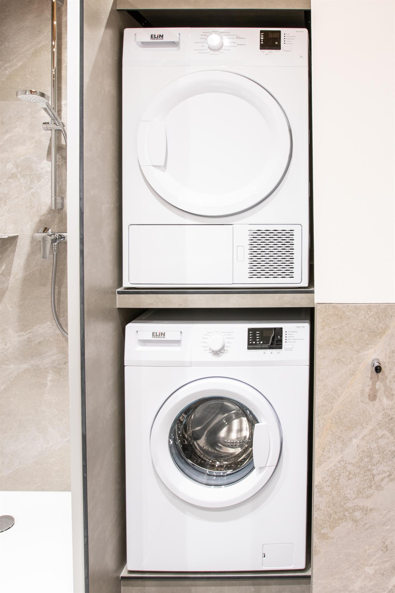 A modern washing machine and a dryer are installed one above the other in a bright and modern apartment. Both appliances are in white and fit well into the surroundings.