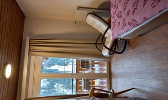 A cozy room with a single bed and a rocking chair. A large window offers a view of a balcony and the surrounding nature.