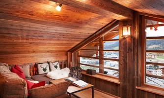 Cozy corner under the roof at the "hayloft" with panoramic views. This charming retreat under the roof offers a wonderful view over the valley and the surrounding mountains. The comfortable couch with fluffy blankets and pillows in alpine style invites you to read, relax, or dream. Warm wood tones, the rustic roof beams, and loving details like the deer cushions and indirect lighting create a soothing feel-good atmosphere. The perfect place for quiet moments after an active day in nature.