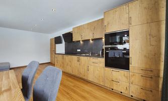 A modern kitchen with wooden cabinets and an elegant countertop. The dining area features a large wooden table and comfortable chairs.