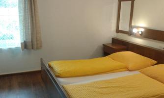 A simple bedroom with a double bed and yellow bed covers. A window lets in natural light.