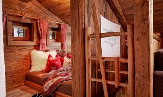 Cozy corner in the hayloft – retreat with cabin charm. A true feel-good highlight: This lovingly designed cozy corner in the hayloft invites relaxation with soft cushions, fluffy blankets, and a rustic wooden ambiance. Framed by traditional red checkered curtains and small casement windows, this retreat offers a sense of security – perfect for reading, dreaming, or simply unwinding.