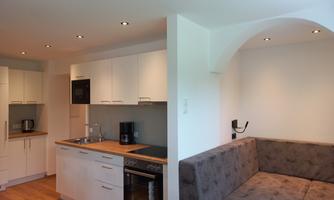 A modern kitchen with white cabinets and a wooden workspace. A cozy seating area with a gray sofa complements the space.