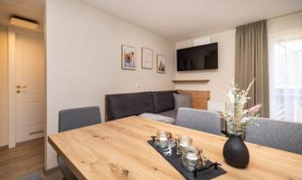 A modern living room with a cozy sofa and a wooden dining table. A television is installed in the living sleeping area.