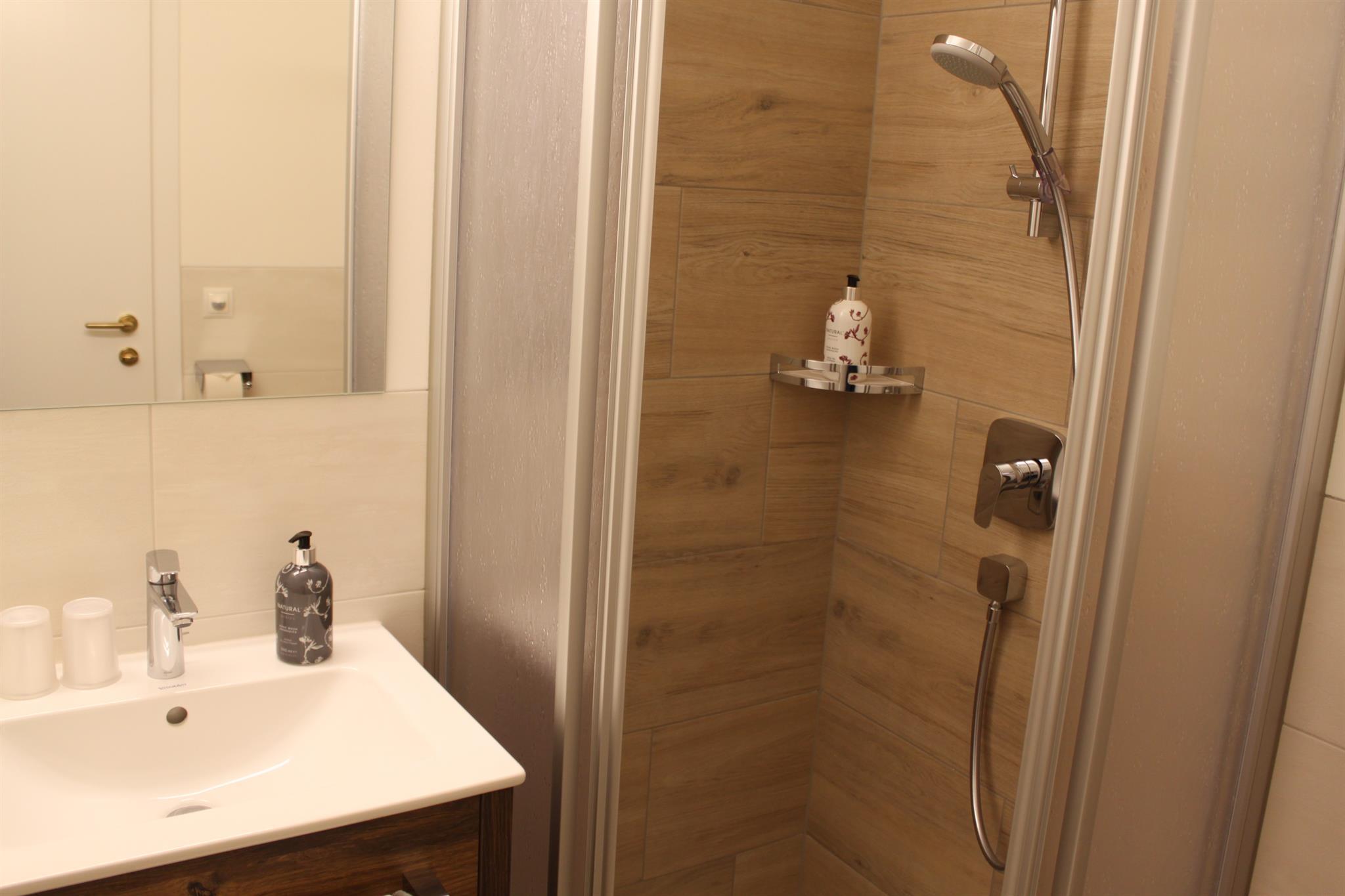 A modern bathroom with a shower and a sink. The walls are light and the wood look creates a cozy atmosphere.