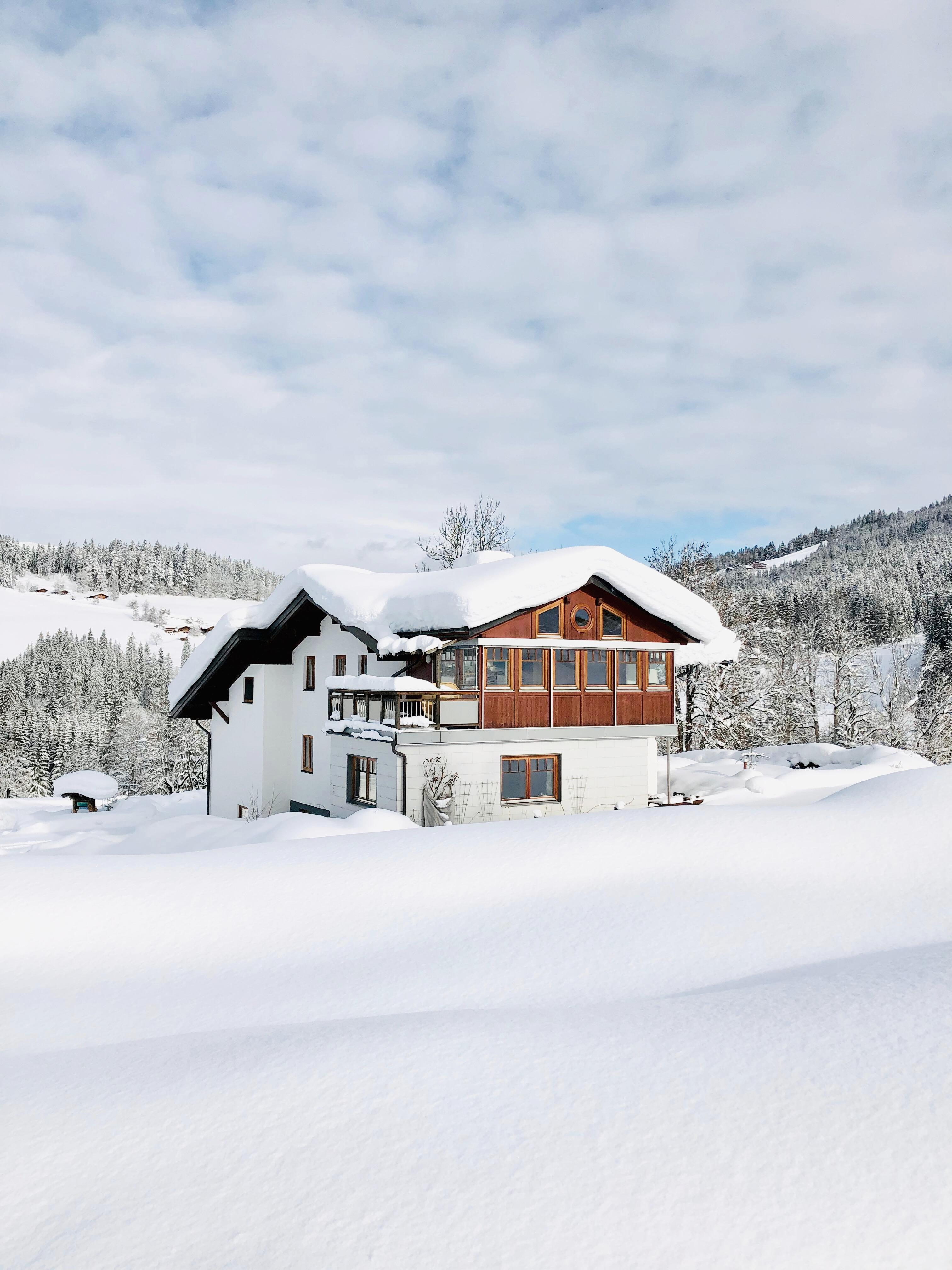 A charming house in a snowy landscape. The surroundings are covered with a thick layer of snow, and the clouds are bright and friendly.