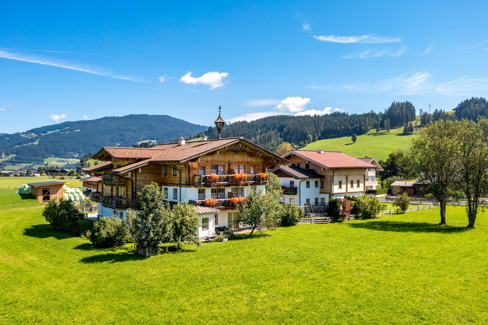 A picturesque farmhouse surrounded by green meadows and gentle hills. The bright blue sky adds a friendly atmosphere to the landscape.