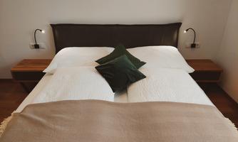 A cozy double bed with white bed linens and decorative pillows. Next to the bed are two nightstands with wall lamps.