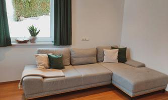 A modern, gray sofa is in a bright room. Next to the window, there is a plant on the windowsill.