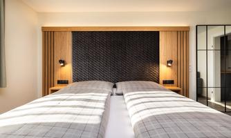 A modern bedroom with two beds and a stylish wooden paneling. The walls are light and the lighting is soft and cozy.
