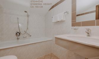 A modern bathroom with a bathtub and a sink. Please note that in the bathtub with hand shower there is only a standing height of approx. 165 cm.