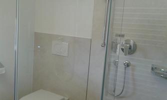 A modern bathroom with a shower partition and toilet. The walls are painted in light tones.