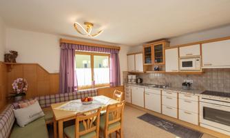 A bright kitchen with a dining area and a large window. The space is cozy, equipped with wood details and modern appliances.