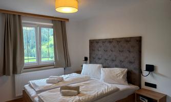 A modern bedroom with a double bed. Large windows provide a view of the green landscape outside.