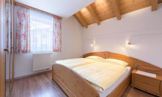 A cozy bedroom with wooden furniture and a double bed. The large window provides plenty of daylight and there is a television in the bedroom.