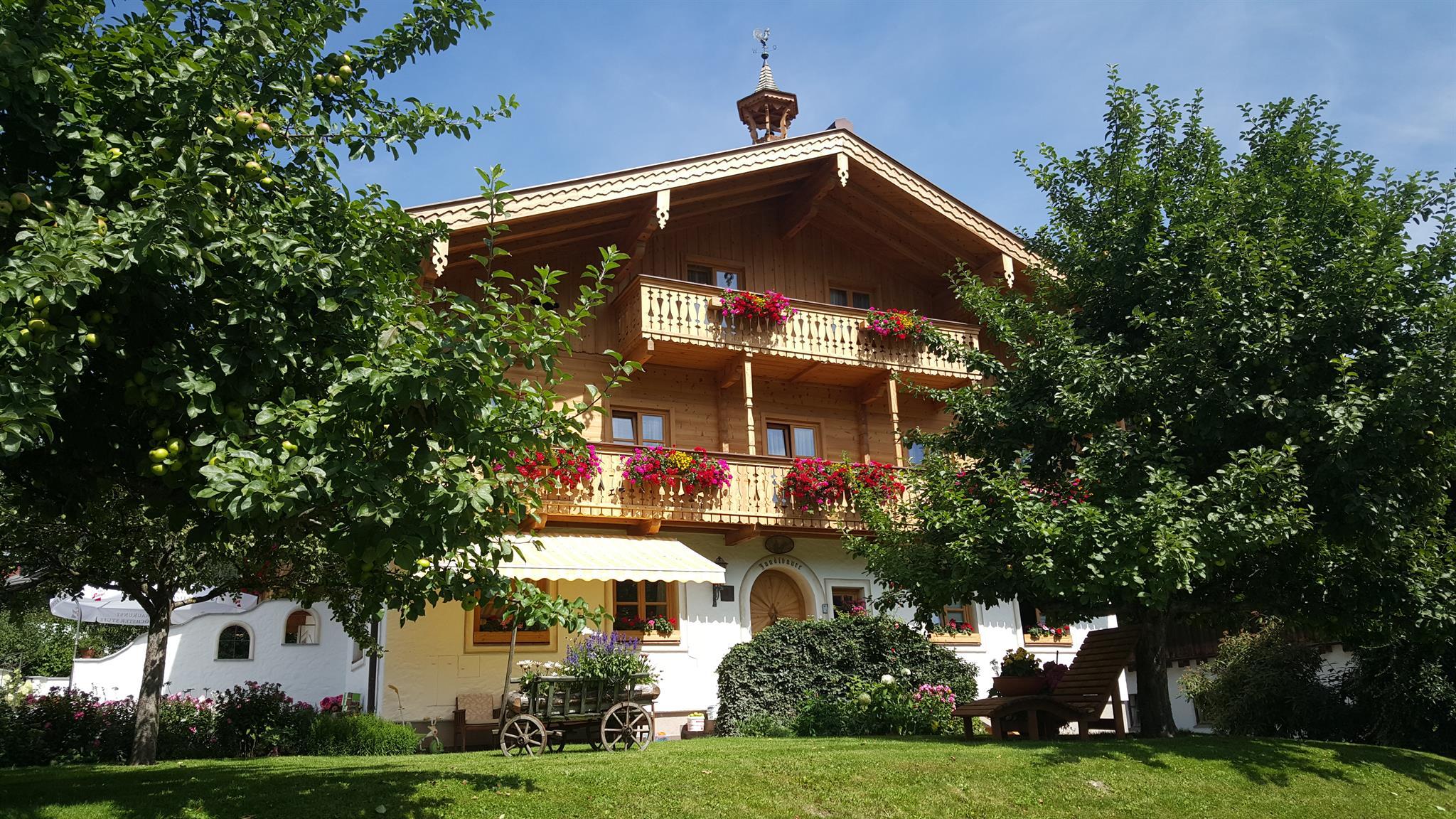 A charming wooden house with balconies, adorned with blooming flowers. Surrounded by lush greenery and trees.