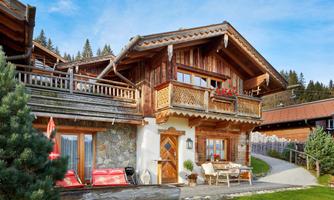 Tradition meets comfort – chalet with balcony, sun terrace, and alpine flair. This exterior view shows the chalet in all its glory: with a lovingly carved wooden balcony, colorful flower boxes, and an inviting terrace with a cozy bench. The combination of natural stone, reclaimed wood, and traditional elements gives the house its unique character. Sun loungers, a barbecue area, and a picturesque view make this spot the perfect feel-good oasis amidst the Salzburg mountain world.