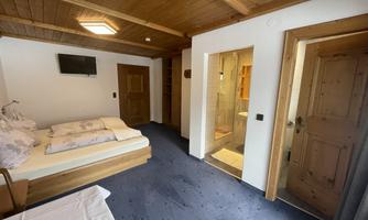 A cozy room with wooden paneling and two beds. There is a TV on the wall and an adjoining bathroom.