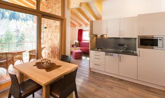 A modern kitchen nook with a wooden dining area. Large windows offer a view of the nature outside.