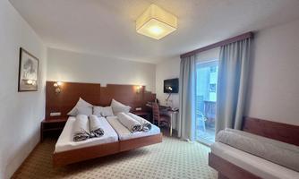 A cozy hotel room with two beds, a television, and a balcony. The walls are light, and the carpet has a simple pattern.