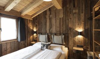 A cozy bedroom with wooden walls and a wooden roof. There are two beds, a window with natural light, and stylish lighting.