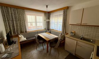 A cozy kitchen with a dining area and large windows. The furniture is simple and functional, with a bright and inviting atmosphere.