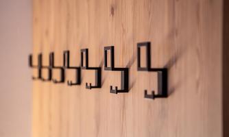 A wooden wall with several black wall hooks in a straight line. The hooks have a modern design and are functional.