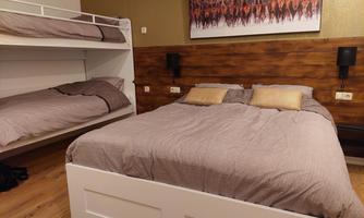 A modern bedroom with a double bed and a bunk bed. The walls are designed in warm colors, and a piece of art adorns the wall above the bed.