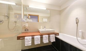 A modern bathroom with a shower, bathtub, and a sink on a wooden shelf. Bright tiles and towels give the room an elegant atmosphere.