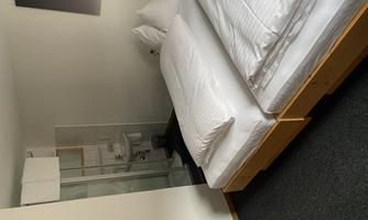 A simple room with two single beds and a modern bathroom. The walls are bright, and the floor is carpeted.