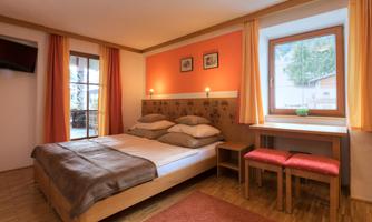 A cozy bedroom with a double bed and a large window. The walls are painted orange, and there is a seating area with chairs.