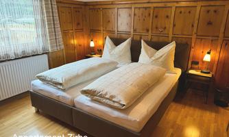 A cozy bedroom with a double bed and decorative pillows. The wooden walls and warm light create an inviting atmosphere.