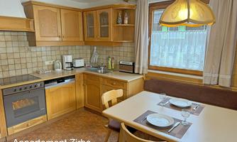 A cozy kitchen with wooden cabinets and a dining table for four people. The room is bright and inviting, perfect for shared meals.